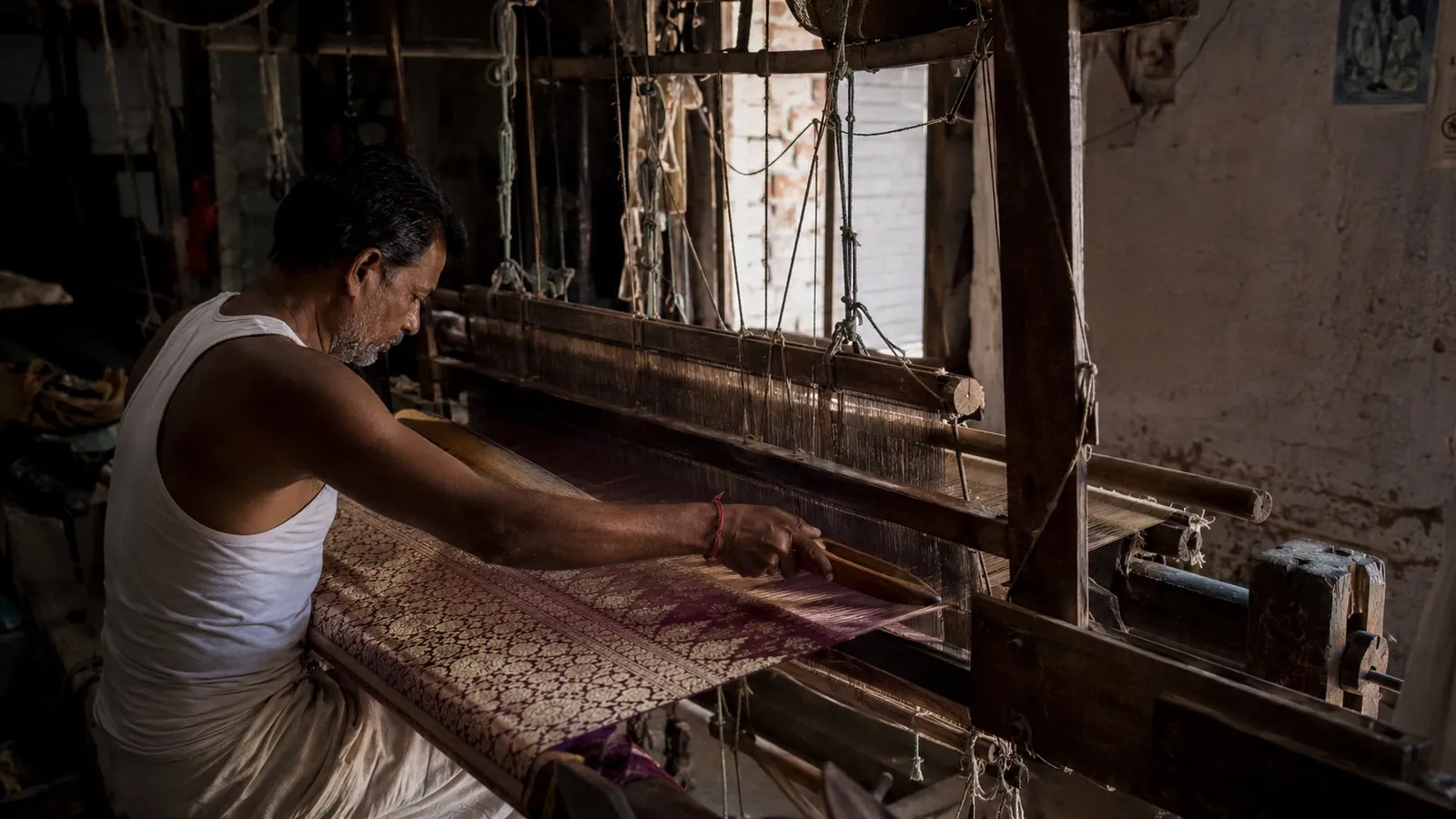 A weaver at a traditional pit-loom in Banaras working on a Vermilion silk panel